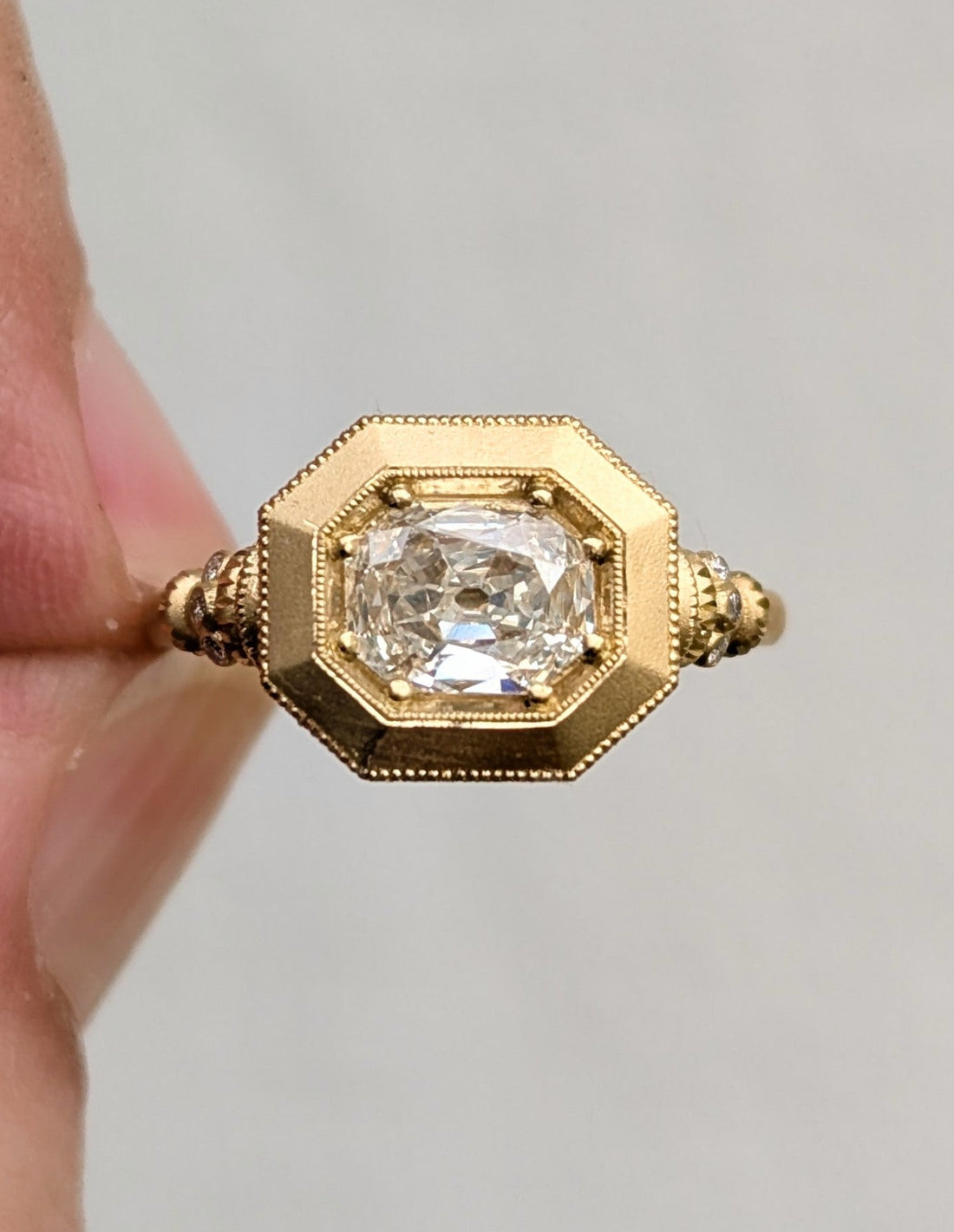 Gold ring with a diamond held by a hand against a gray background